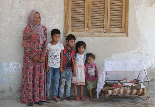 Portrait of Widad who stands next to her five children.